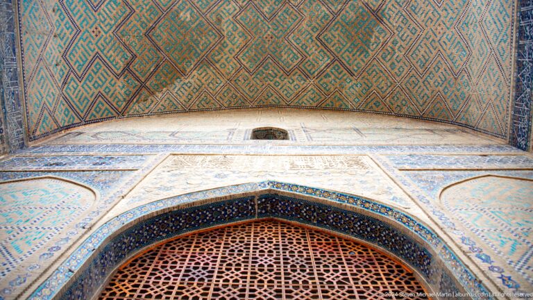 Upward view of a portal with reddish lattice, pale patterned walls, blue borders, and a green geometric vault.