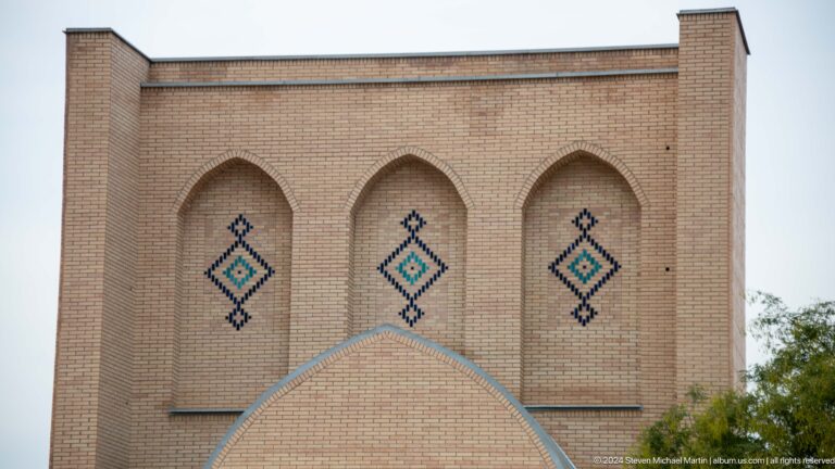 Plain buff-brick façade with three shallow pointed recesses and narrow blue diamond tile motifs.