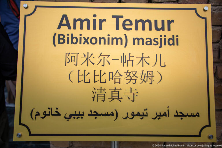 Yellow multilingual site sign reading 'Amir Temur (Bibixonim) masjidi' with Chinese and Arabic-script text.