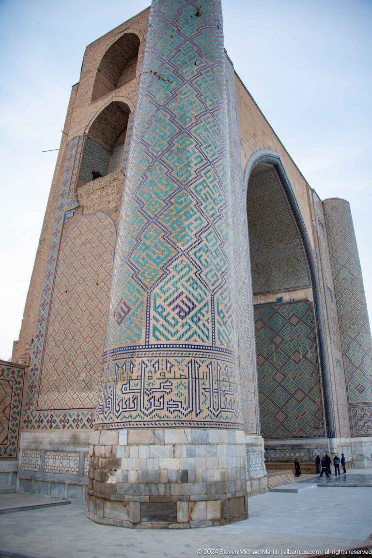 Steep upward view of a massive tiled portal pier with turquoise geometric bands and a calligraphic panel.