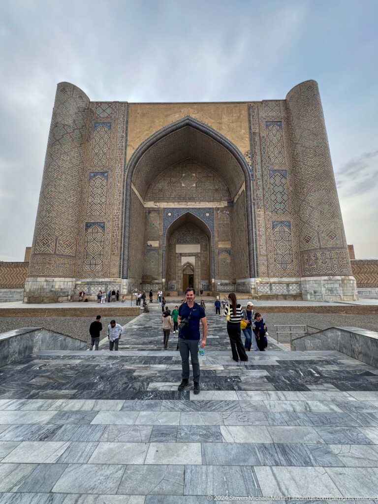 Visitor standing on the paved approach before the enormous pointed iwan of the Bibi-Khanym Mosque.
