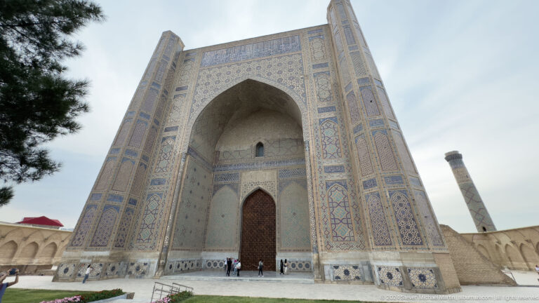 Low-angle frontal view of a tall pointed portal with blue tile borders and tiny visitors at its base.