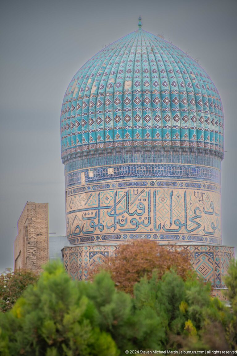 Close-up of a cylindrical tower with a large turquoise calligraphic tile band and blue-green upper tiles.