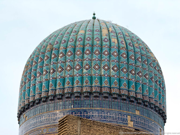 Turquoise ribbed mosque dome with repeated dark motifs, a small finial, and a patterned base band.
