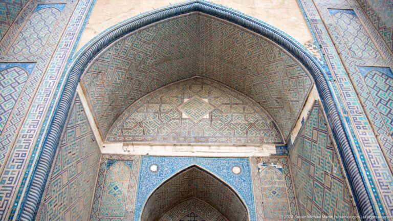 Upward close view of a pointed iwan vault covered in green geometric pattern and blue tile borders.