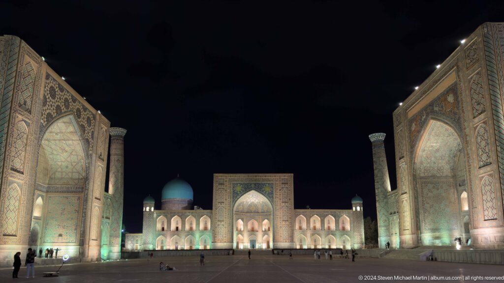 Quiet nighttime view of Tilya-Kori Madrasa framed by the side madrasas across an almost empty square.
