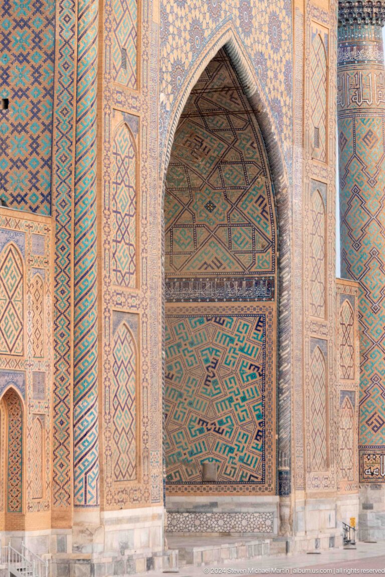 Close view of a pointed portal recess beside turquoise and ochre geometric tile panels.