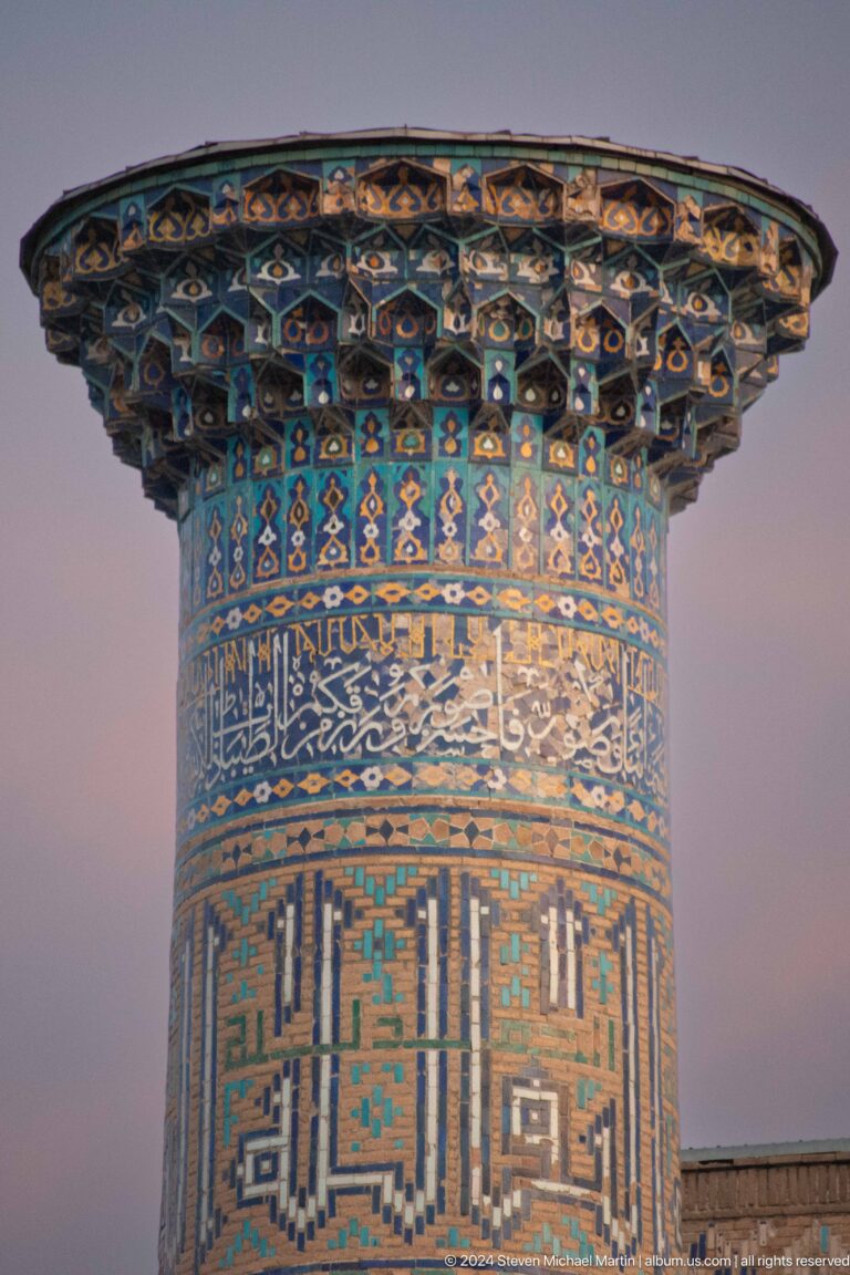 Close-up of a tiled minaret crown with a broad blue calligraphic band.