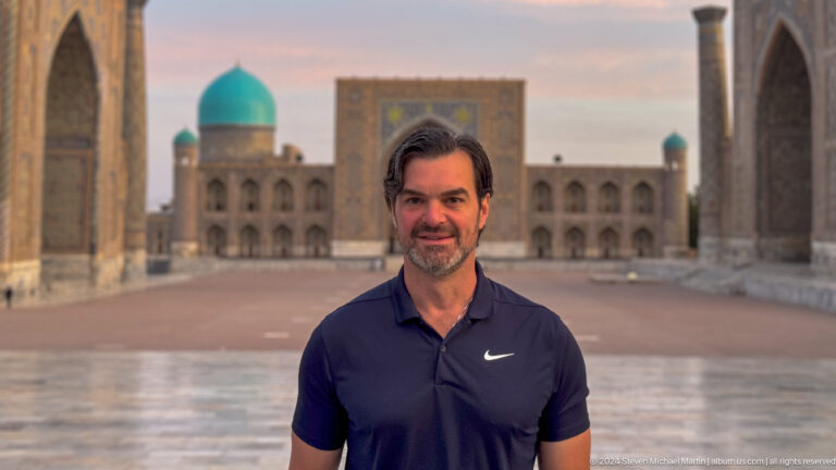 Male traveler in a dark polo shirt standing before the blurred architecture of Registan Square.
