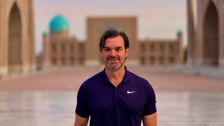 Close portrait of a male traveler with a blurred Registan madrasa behind him.
