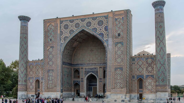 Frontal view of Ulugh Beg Madrasa with a monumental tiled portal and two slender minarets.