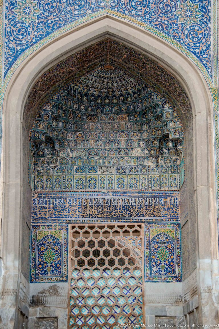 Muqarnas canopy above a blue calligraphic band and wooden lattice screen.