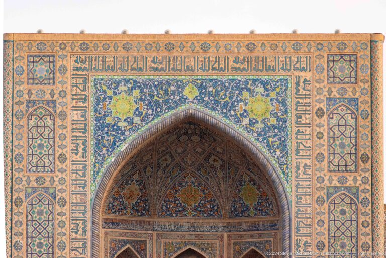 Close view of a Tilya-Kori portal with Arabic inscription, blue floral tilework, and layered geometric borders.