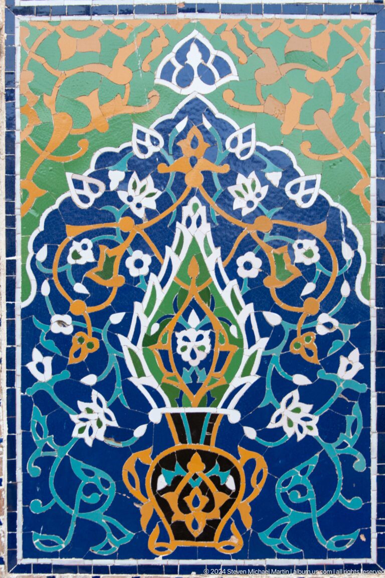 Close-up of a green, white, orange, and turquoise floral motif on dark-blue tilework.