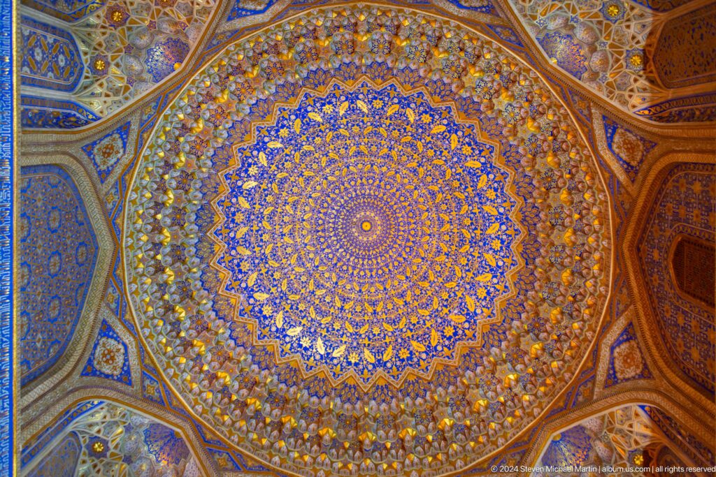 Upward view of a circular blue-and-gold decorated dome ceiling inside the Registan.