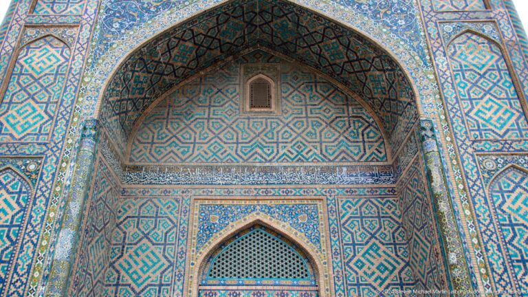 Turquoise tiled pointed arch with a small upper opening and recessed doorway at the Registan.