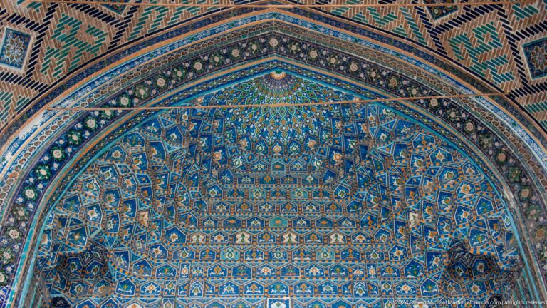 Close-up of a blue tiled semi-dome covered with dense repeating geometric and floral motifs.
