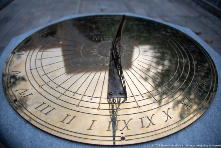 Polished brass sundial with a triangular gnomon, engraved hour lines, and Roman numerals.