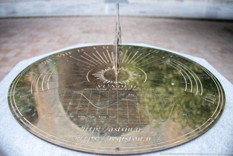 Round brass sundial engraved with curved hour lines, inscriptions, and a map-like central design.