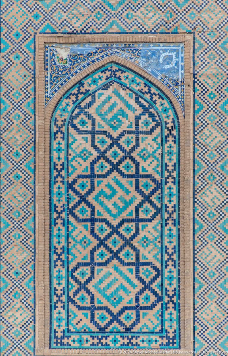Arched tile panel with turquoise, blue, white, and ochre geometric patterns.