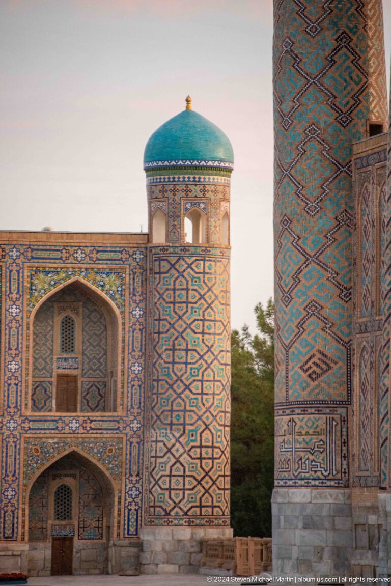 Tiled pointed arch beside a cylindrical minaret covered in geometric patterns.