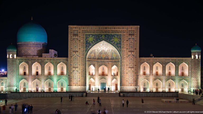 Illuminated Tilya-Kori Madrasa at night with a central portal, arcades, and turquoise dome.
