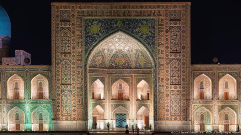 Illuminated main portal of Tilya-Kori Madrasa with stacked niches and richly patterned tilework.