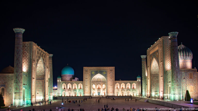 Wide nighttime view of Registan Square with Tilya-Kori centered between the two flanking madrasas.
