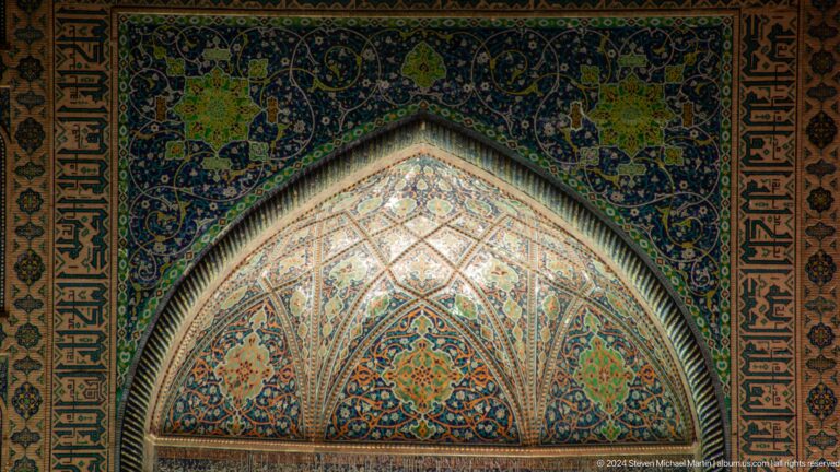 Close-up of an illuminated pointed portal half-dome covered with colorful floral arabesques.