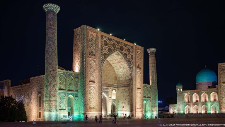 Illuminated Ulugh Beg Madrasa at night with its monumental portal and twin minarets.
