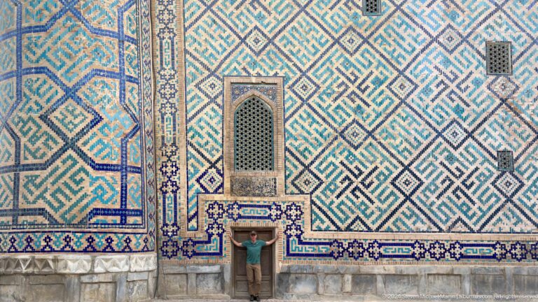 Visitor standing in a small doorway beneath a large blue-and-white geometric tile facade.