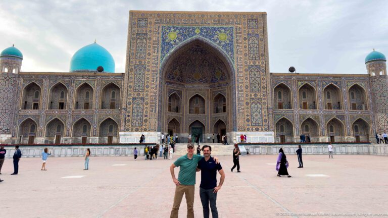 Two men posing together in Registan Square with Tilya-Kori Madrasa behind them.