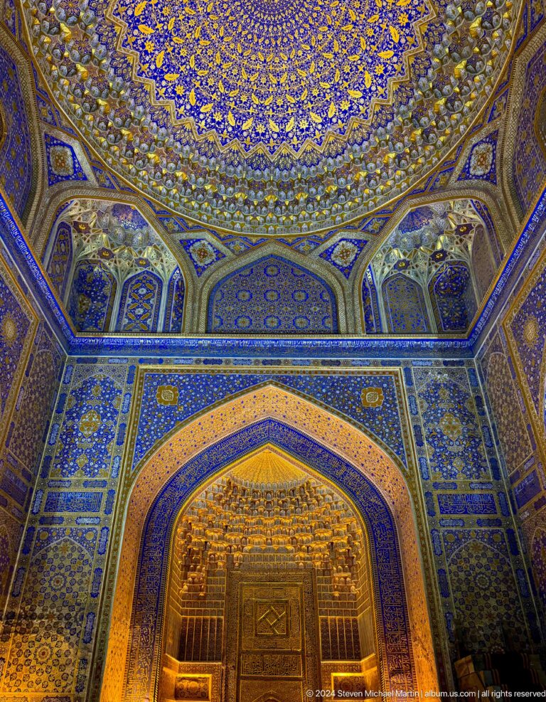 Wide view of Tilya-Kori's blue-and-gold interior with a gilded arch and decorated ceiling transitions.