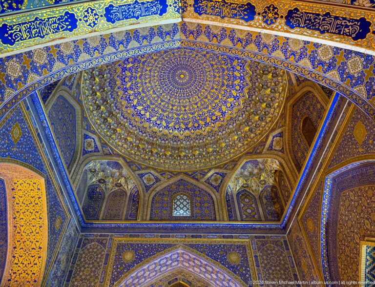 Oblique upward view of a gilded dome surrounded by blue patterned walls and arched transition bays.