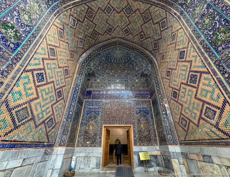 Monumental tiled pointed recess framing a small doorway with a silhouetted visitor.
