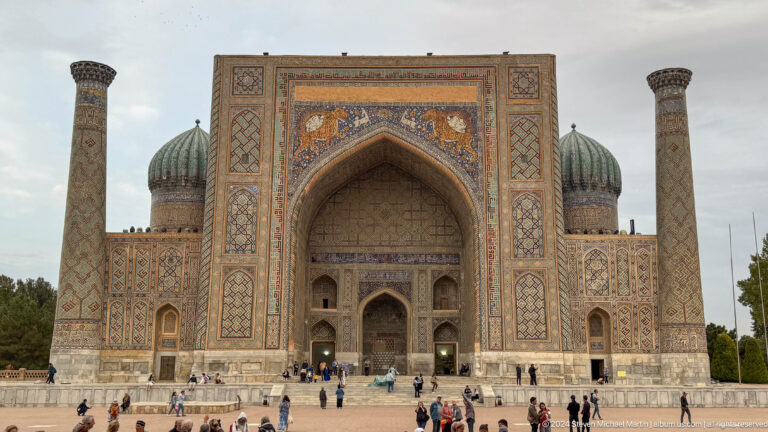 Frontal view of Sher-Dor Madrasa with its monumental portal, ribbed domes, minarets, and feline mosaics.