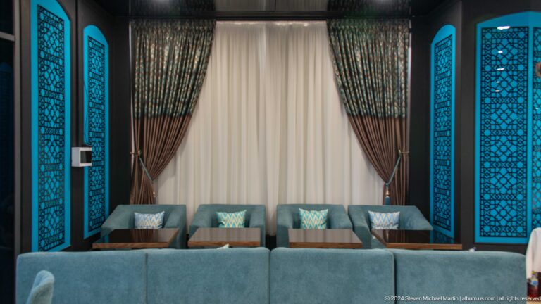 Four teal lounge chairs beneath tall patterned curtains and turquoise decorative wall panels.