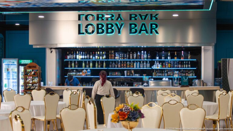 Staffed hotel lobby bar beneath large turquoise English and Cyrillic signage.