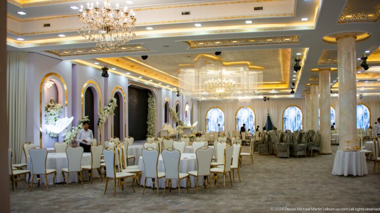 Bright banquet hall with crystal chandeliers, white-and-gold chairs, and floral arch decorations.