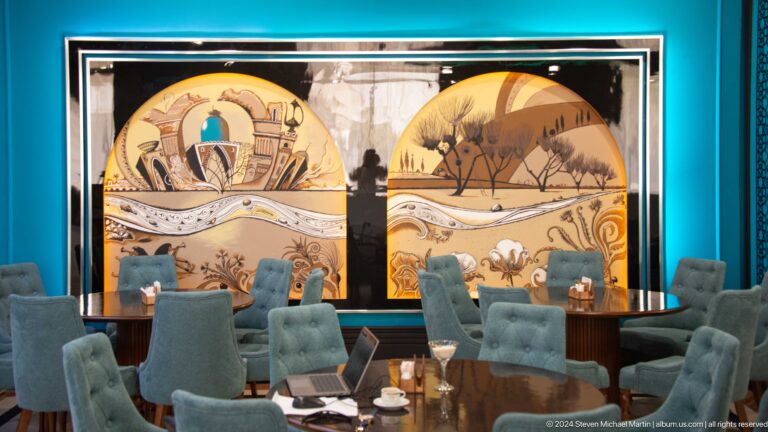 Teal dining chairs beneath two arched murals showing monumental architecture and a desert landscape.