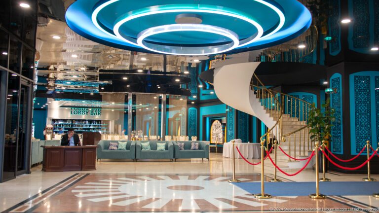 Wide Hotel Uzbekistan lobby with circular ceiling lights, teal sofas, curved staircase, and red ropes.