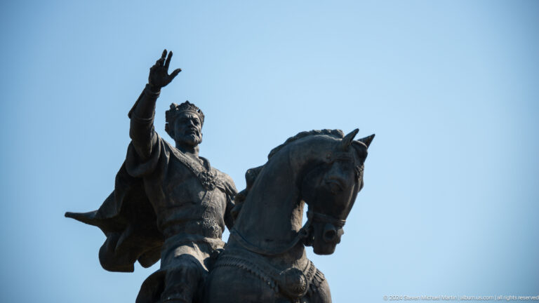 Close upward view of Amir Timur raising one hand while mounted on a bronze horse.