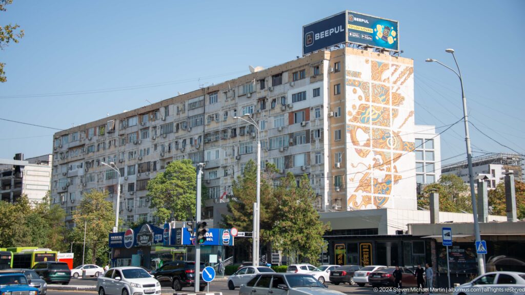 Long apartment block with many balconies and a colorful mosaic covering its end wall.