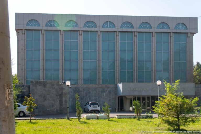 Modern museum building with tall glass bays, arched window tops, and a dark stone base.