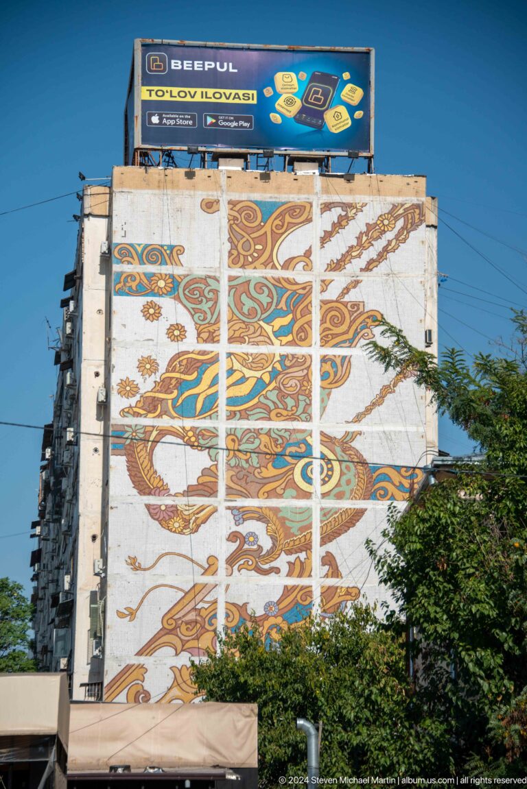 Close view of colorful floral and vegetal motifs in a tiled apartment-wall mosaic.
