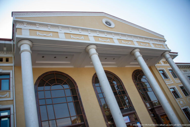 Low-angle view of a cream public building with giant white columns and tall arched windows.