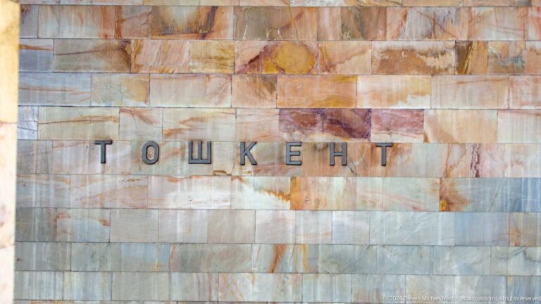 Cyrillic letters spelling ТОШКЕНТ mounted on a warm multicolored marble wall.