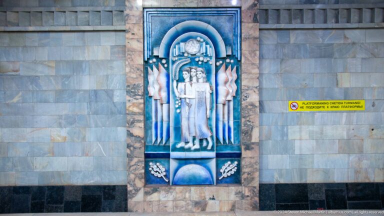 Tall blue ceramic relief showing three women beneath an arch at Toshkent Metro station.