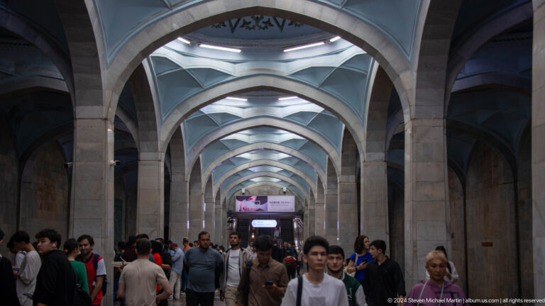 Crowded metro passage with repeated pointed arches and faceted white ceiling vaults.