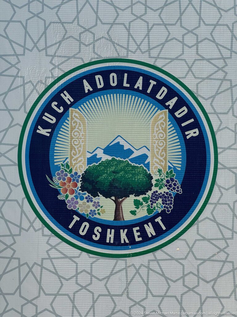 Round Tashkent mosaic emblem with a tree, mountains, grapes, flowers, and Uzbek inscription.